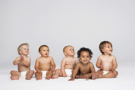 Row of multiethnic babies sitting side by side looking away isol